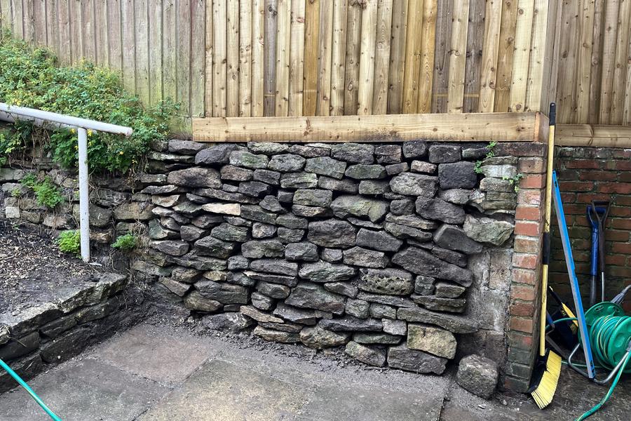 A rebuilt dry-stone retaining garden wall with new fencing above