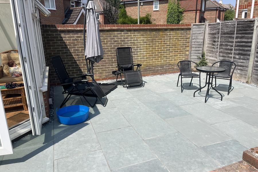 A finished porcelain patio with garden furniture, enclosed by a brick wall and fencing